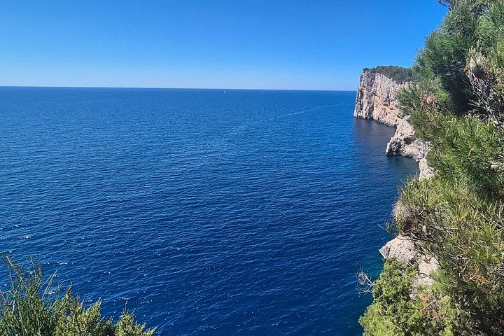 Blick auf das tiefblaue Meer und eine zerklüftete Küste mit Klippen.