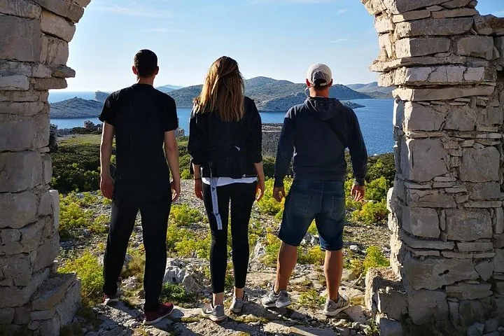 Drei Personen stehen an einer Steinruine und blicken auf die Inseln des Nationalparks Kornati.