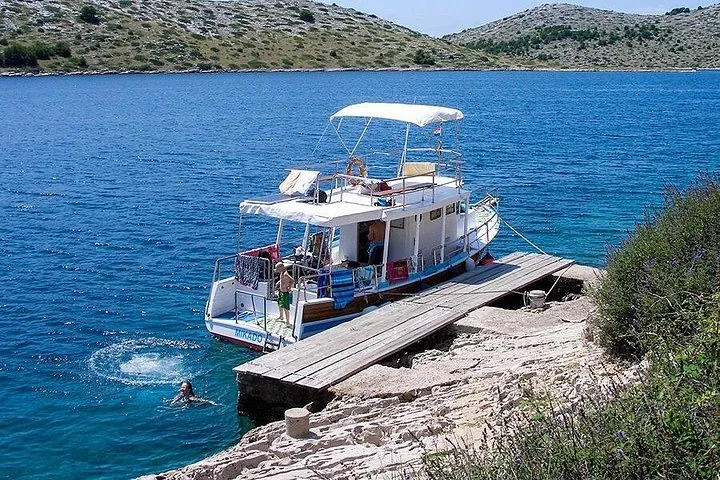 Un barco de excursiones blanco amarrado a un muelle de piedra en una bahía resguardada.