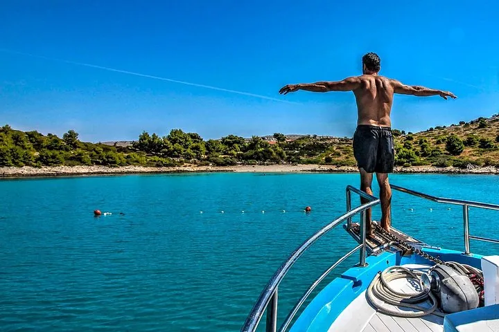 Un hombre está de pie en la proa de un barco con los brazos extendidos.